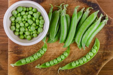 Taze bezelye ve bezelye kabukları. Kavanozda bezelye ve tahta tahtada bezelye kabukları. Üst görünüm.