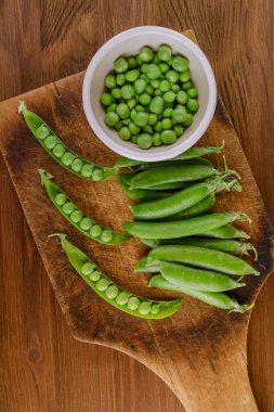 Taze bezelye ve bezelye kabukları. Kavanozda bezelye ve tahta tahtada bezelye kabukları. Üst görünüm.