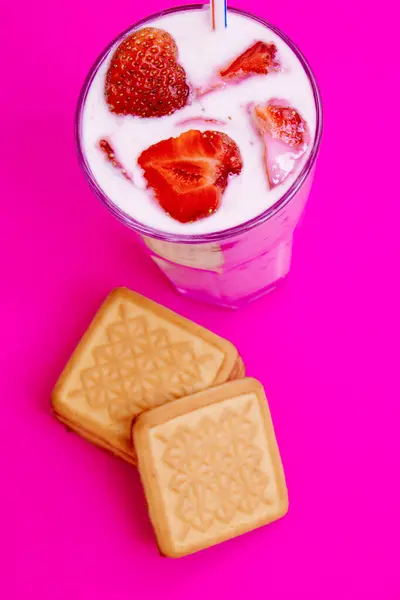 Glass of strawberry yogurt with cookies on pink background. Strawberry yogurt covered by fresh strawberry slices.