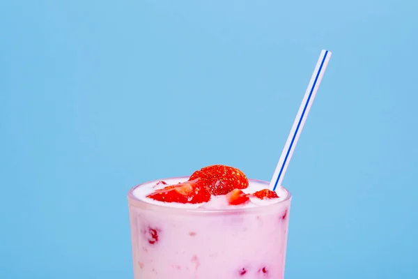 Glass of strawberry yogurt on blue background. Strawberry yogurt covered by fresh strawberry slices.
