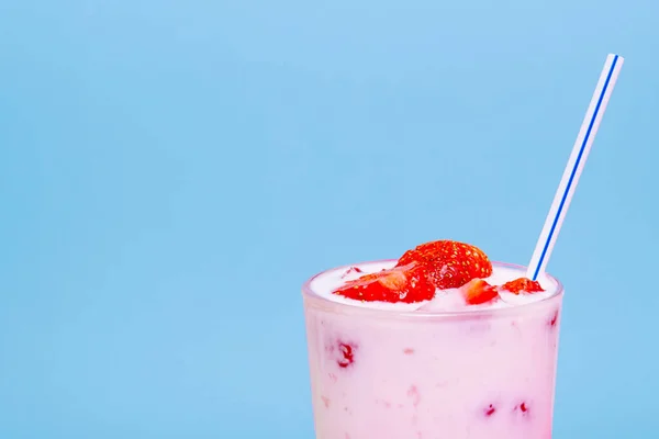 Glass of strawberry yogurt on blue background. Strawberry yogurt covered by fresh strawberry slices.