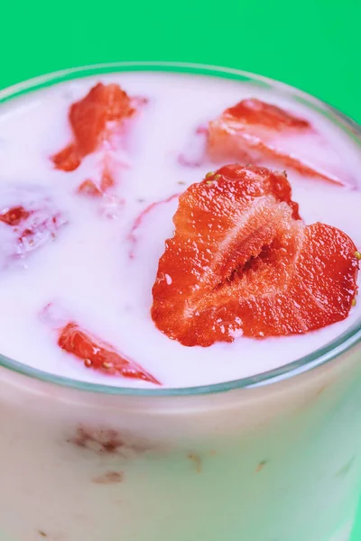 Glass of strawberry yogurt covered by fresh strawberry slices. Strawberry yogurt on a green background. Closeup shot.