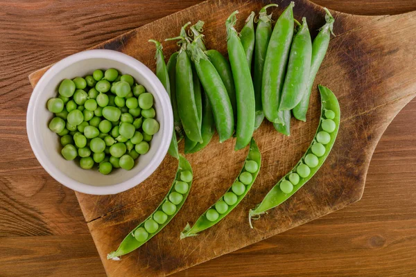 Fresh green pea and pea pods. Pea in bowl and pea pods on wooden board. Top view.