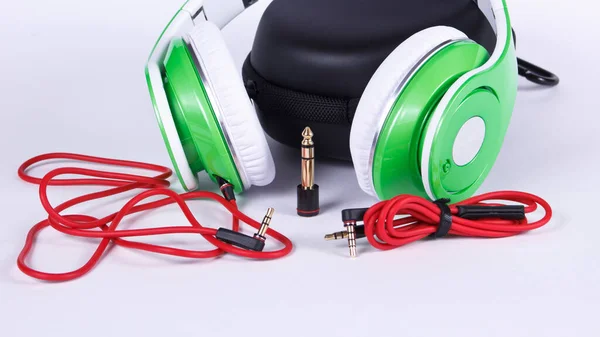 Green headphones with cables and connectors and case lays on light background.
