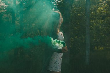 Sis bombası olan kız doymuş yeşil duman bulutları yaratıyor..