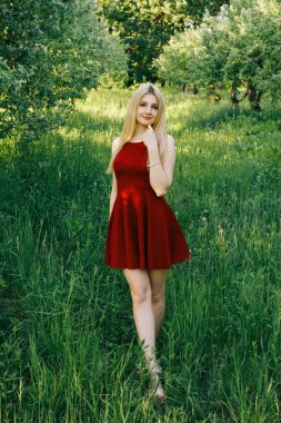 Gün batımında bahçede kırmızı elbiseli, gülümseyen kadın..