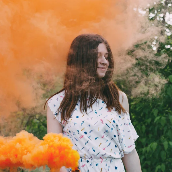 Girl with smoke bomb makes saturated orange clouds of smoke.