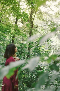 Mor elbiseli güzel esmer kadın ormandaki güneşli havanın tadını çıkarıyor..