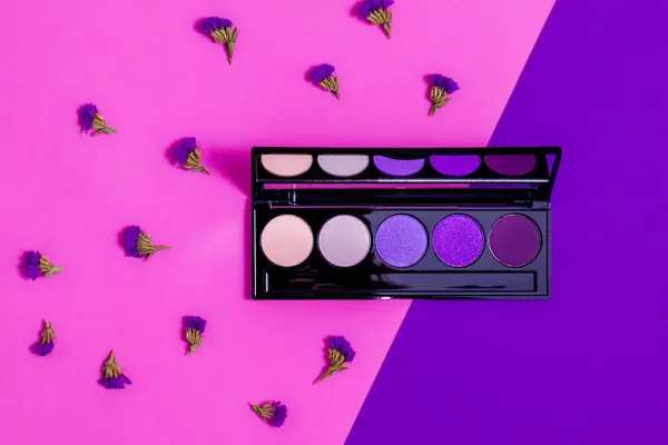 Makeup eyeshadow palette with limonium flowers on the purple and pink background. Makeup eyeshadow palette set.