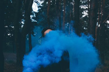 Sis bombası taşıyan kişi ormanda mavi duman bulutları oluşturur. Yumuşak odak.
