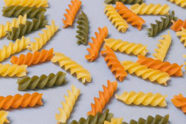 Gri arka planda dağınık üç renkli makarna seti. Yemek deseni. Yakın plan. Üst görünüm.