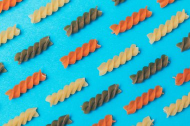 Mavi arka planda üç renkli Fusilli makarnadan yapılmış çizgiler. Yakın plan. Makro fotoğraf. Kavram. Yiyecek deseni.