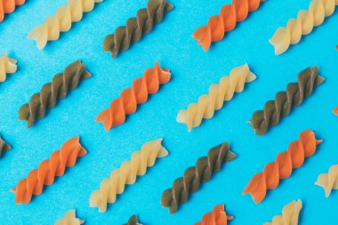 Mavi arka planda üç renkli Fusilli makarnadan yapılmış çizgiler. Yakın plan. Makro fotoğraf. Kavram. Yiyecek deseni.