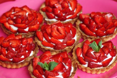 Taze çilekli turtalar tabakta yakın plan. Nane yapraklarıyla süslenmiş tartlar..