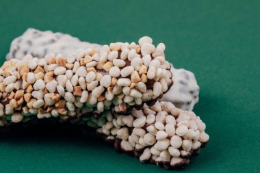 Mısır gevreği, fıstık parçaları ve yeşil arka planda beyaz kremayla kaplı çikolatalar. Makro çekim.