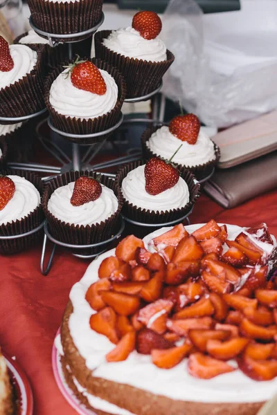 Cake and cupcakes with fresh juicy strawberries on top.