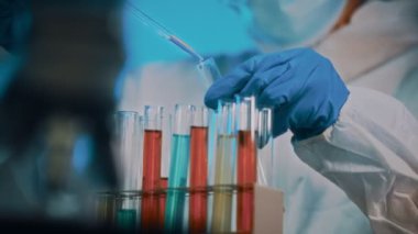 Gözlüklü ve maskeli bir kadın laboratuarda test tüpleriyle çalışıyor..
