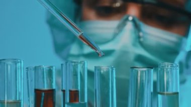 Gözlüklü ve maskeli bir kadın laboratuarda test tüpleriyle çalışıyor..