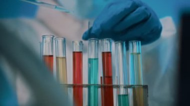 Gözlüklü ve maskeli bir kadın laboratuarda test tüpleriyle çalışıyor..