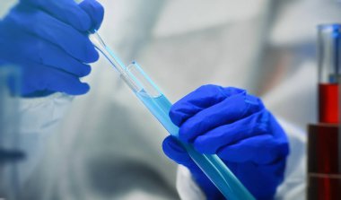 Gözlüklü ve maskeli bir kadın laboratuarda test tüpleriyle çalışıyor..