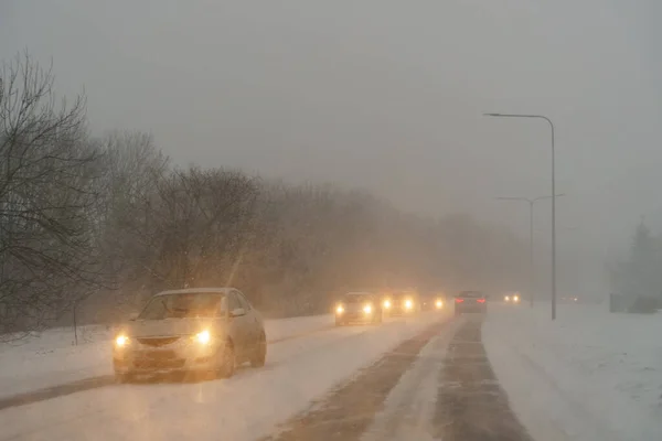 Cars drive on the road in difficult weather conditions. Blizzard.