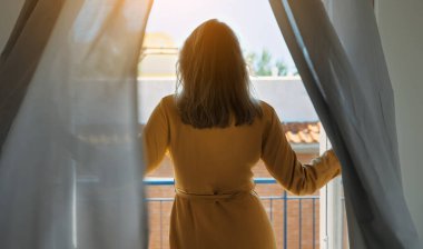 Kadın pencerenin önünde dururken ılık yaz melteminin tadını çıkarıyor..