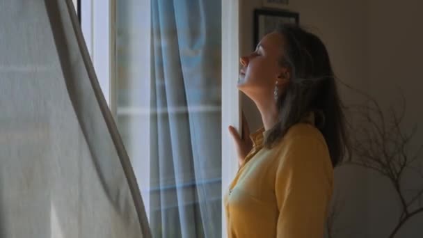 Woman Enjoys Summer Breeze While Standing Front Window — Vídeos de Stock