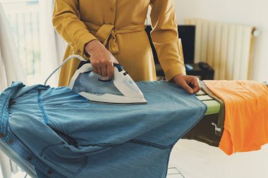 Woman in a yellow dress is ironing clothes.
