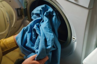 Çamaşır makinesine çamaşır yükleyen kadın.