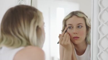 Teenage girl doing makeup with black eyeliner.