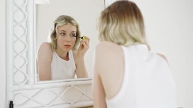 Teenage girl applying black mascara on lashes.
