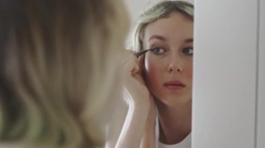 Teenage girl doing makeup with black eyeliner.
