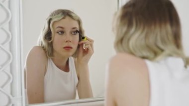 Teenage girl applying black mascara on lashes.