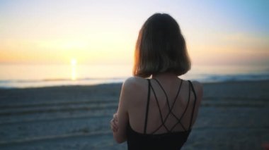 Mother cover his daughter with blanket and hugging on the beach at sunset.