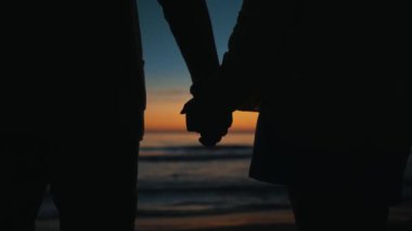 Couple in love holds hands at sunset by the sea.