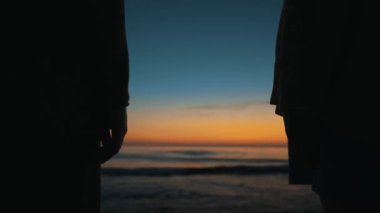 Couple in love holds hands at sunset by the sea.