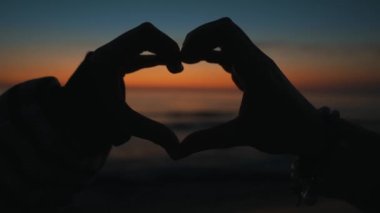 Hands of women made heart shape at sunset.