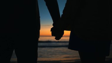 Couple in love holds hands at sunset by the sea.