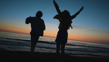 Two girls dance in the evening at sunset by the sea.
