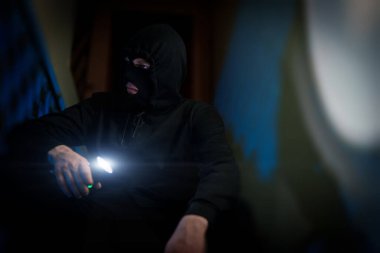 Portrait of thief in balaclava with a flashlight.
