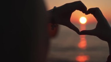 Female hands making heart shape in the sunset.