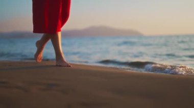 Woman in red dress walks along the beach.
