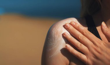 Omzuna güneş kremi süren bir kadın..