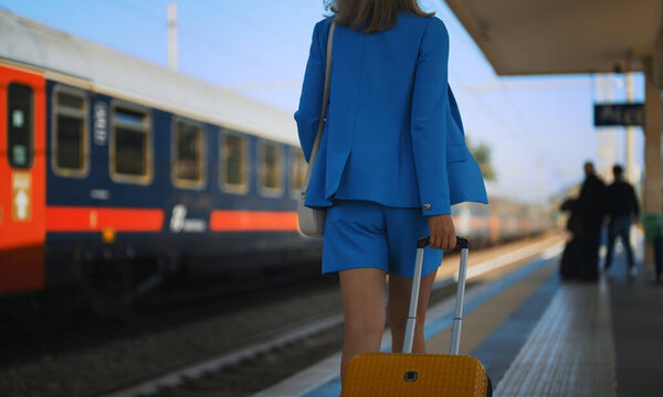 Woman with a suitcase walks along the platform at the train station.