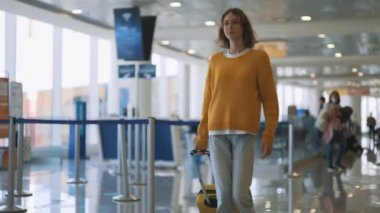 Tween girl with suitcase walking in airport terminal.