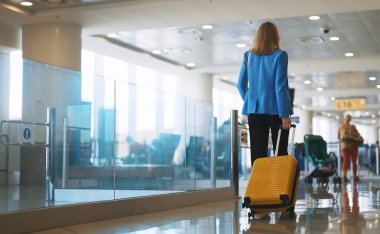 Havaalanı terminalinde bavullu bir kadın yürüyor. Arka plan.