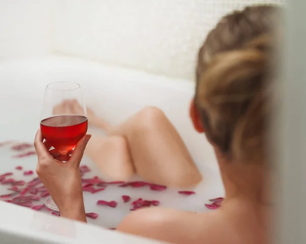 女性はミルクとバラの花びらでお風呂でワインを楽しんでいます — ストック写真
