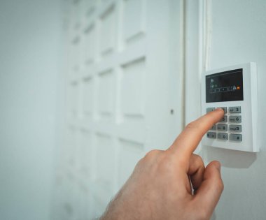 Adam evdeki alarm paneline kod koyuyor.