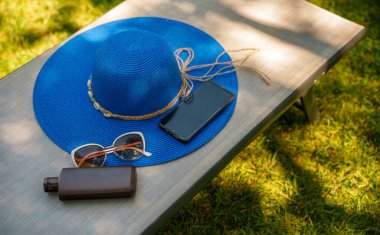 Mavi şapka, güneş kremi, telefon ve güneş gözlüğü..