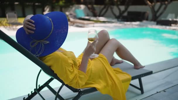 スイミングプールの近くでリラックスしたワインの白いグラスを持つ女性 — ストック動画